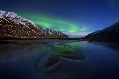 Fine art photograph of the Aurora Borealis Northern Lights with a frozen heart and snowy mountains in north Iceland. Photo by landscape photographer, Serena Dzenis.