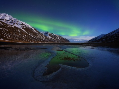 Fine art photograph of the Aurora Borealis Northern Lights with a frozen heart and snowy mountains in north Iceland. Photo by landscape photographer, Serena Dzenis.